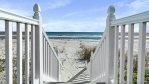 A wooden staircase leading to a sandy beach with ocean views.