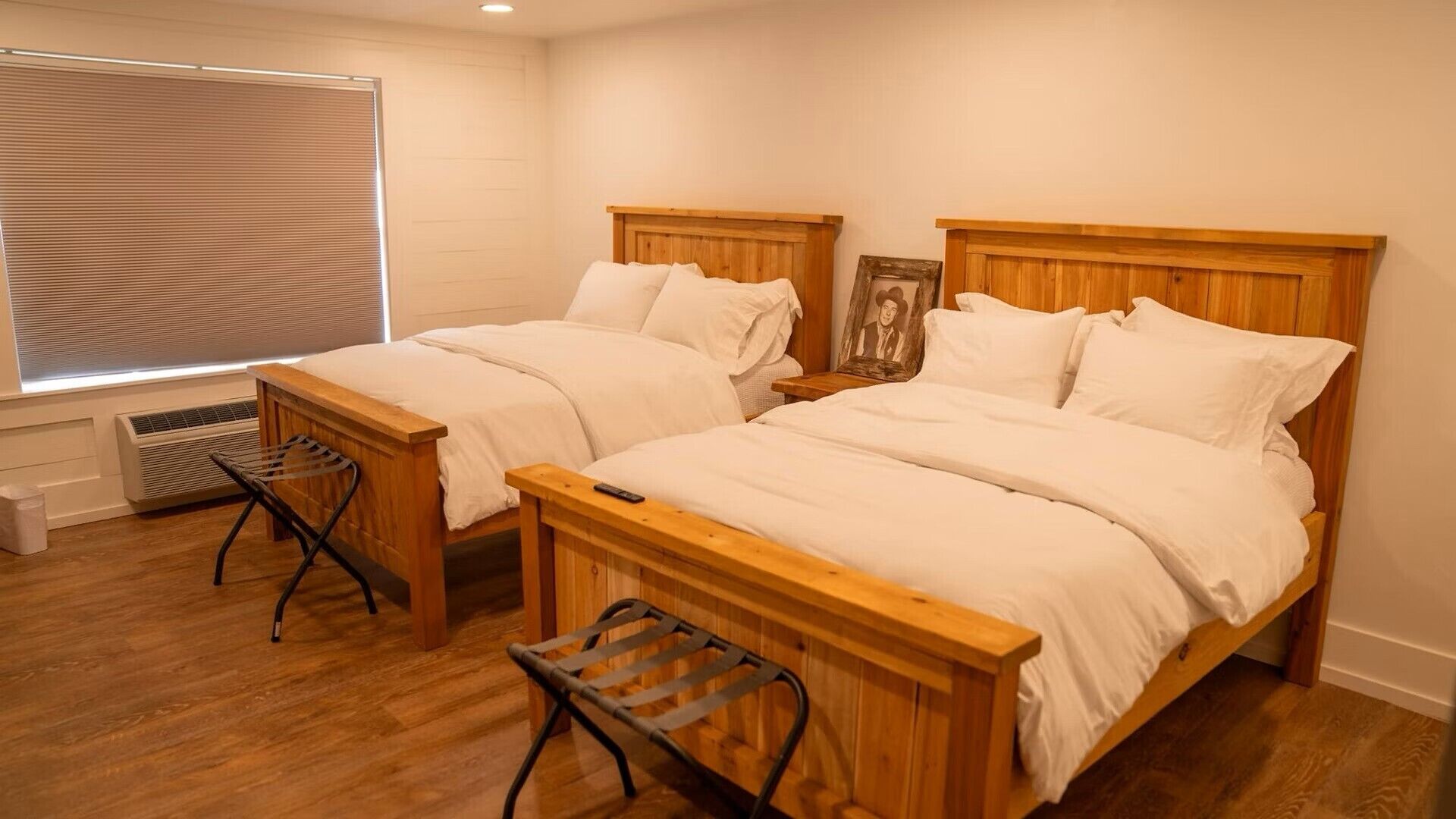 A bedroom with two wooden beds, a window with blinds, a radiator, and a small stool.