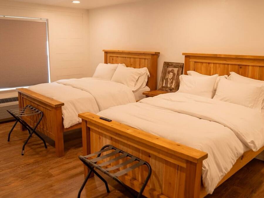 A bedroom with two wooden beds, a window with blinds, a radiator, and a small stool.
