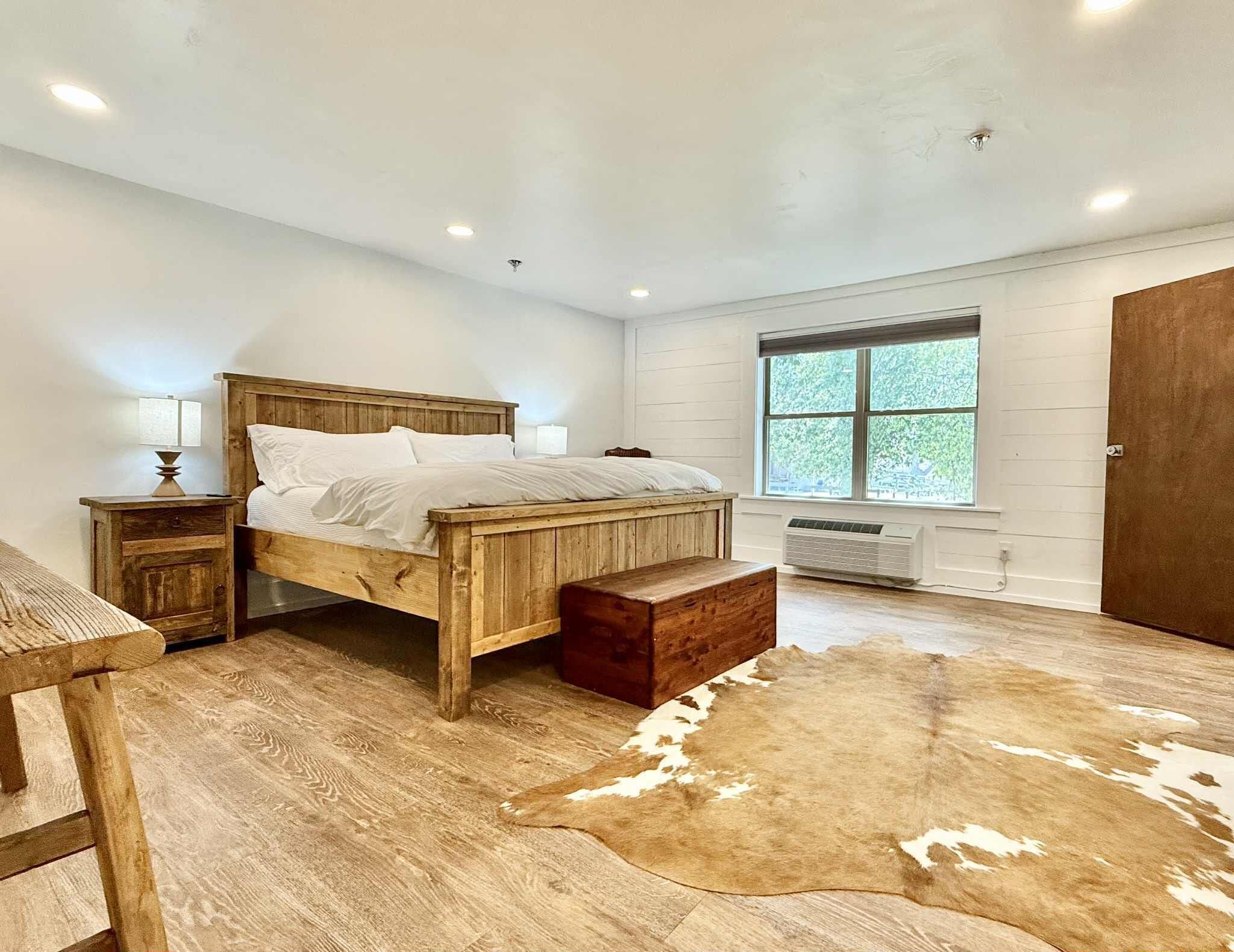 A bedroom with a wooden bed, a nightstand, a window with a view, and a cowhide rug.