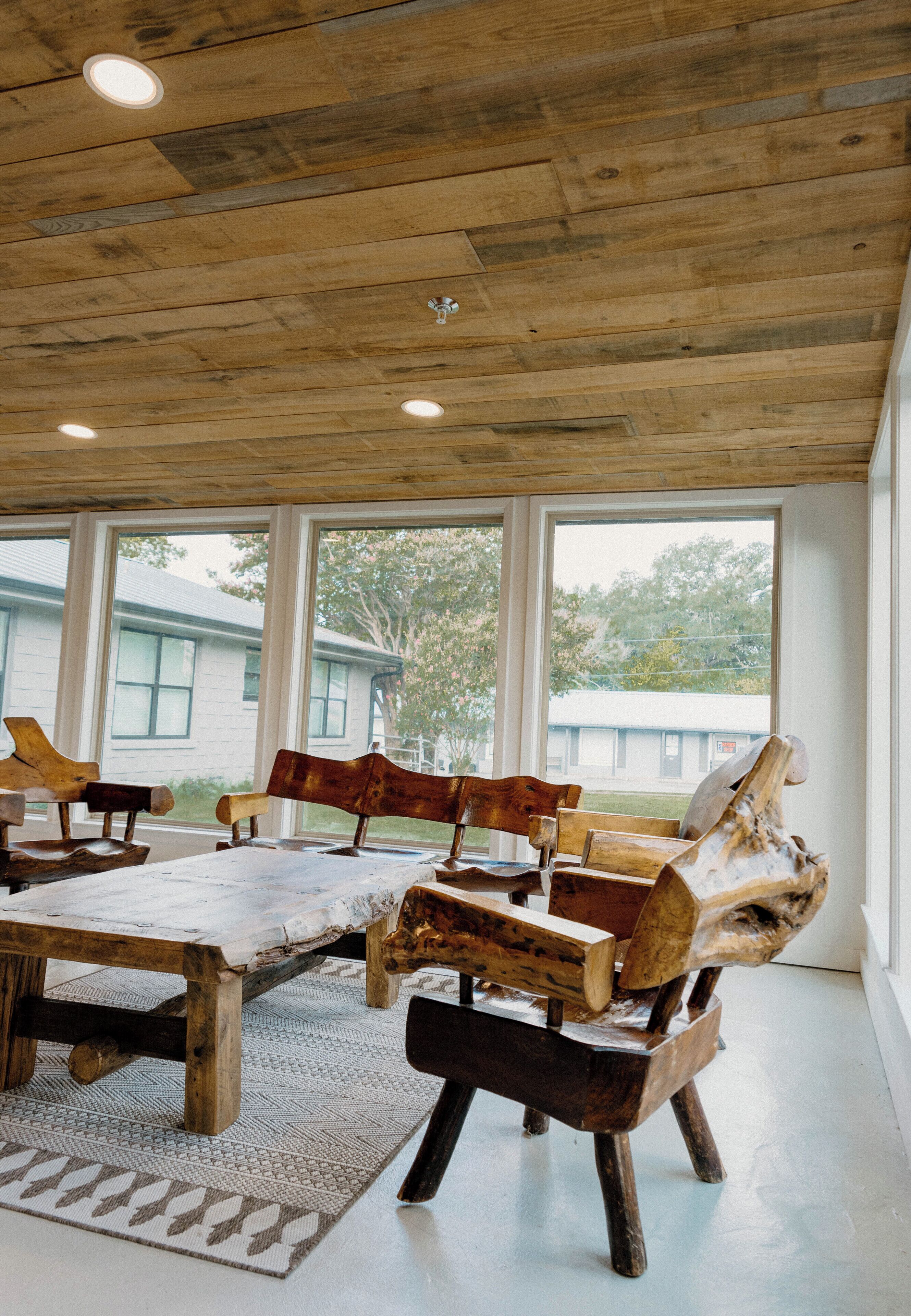 Un intérieur rustique avec des meubles en bois, de grandes fenêtres et une vue sur une maison à l’extérieur.