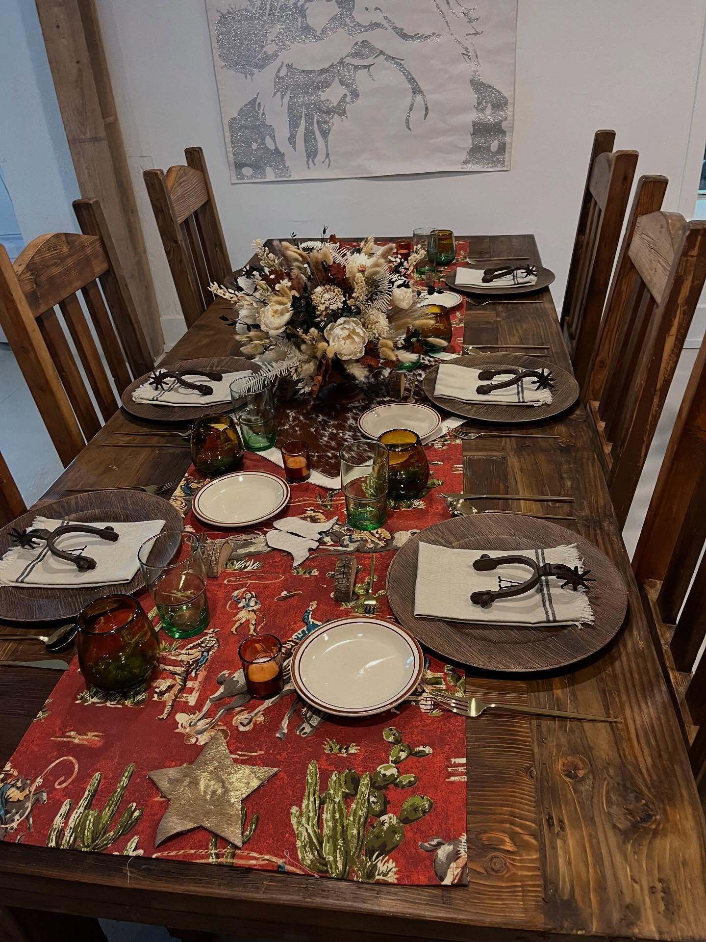 Ein Holztisch ist gedeckt mit Tellern, Besteck und einer Blumenarragemement.