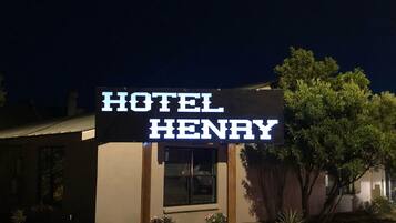 Señalización de 'Hotel Henry', con vista clara a la entrada del edificio y un árbol al fondo.