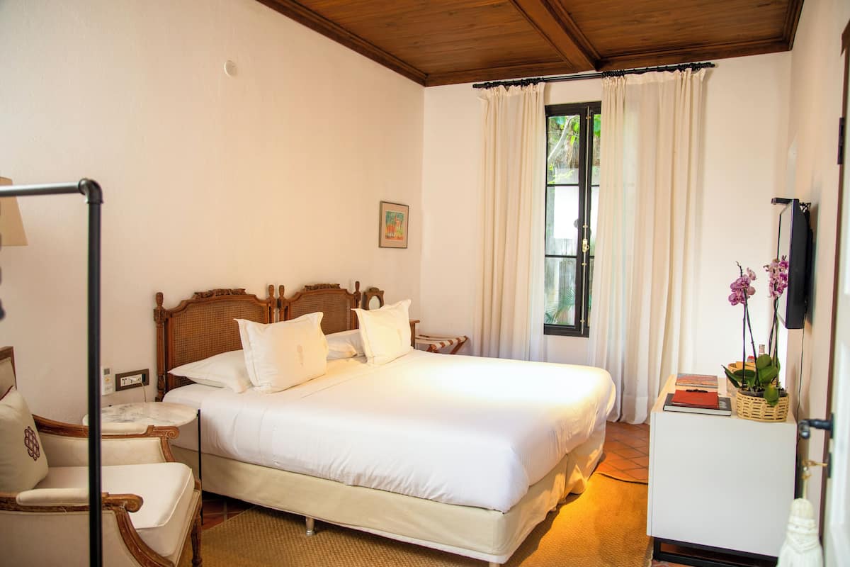 Un dormitorio ordenado con una cama grande, una mesita de noche, una silla y un mueble pequeño.