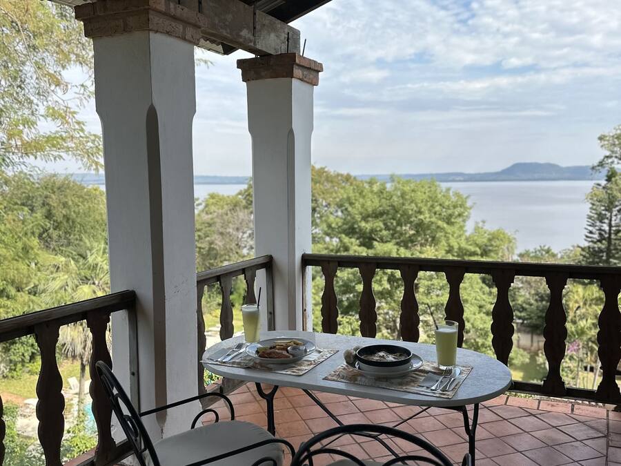 A terrace with a table set for two, overlooking a body of water and greenery.