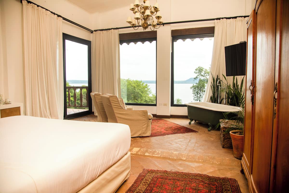 Un dormitorio con una cama grande, un sillón, una bañera y vistas al exterior.