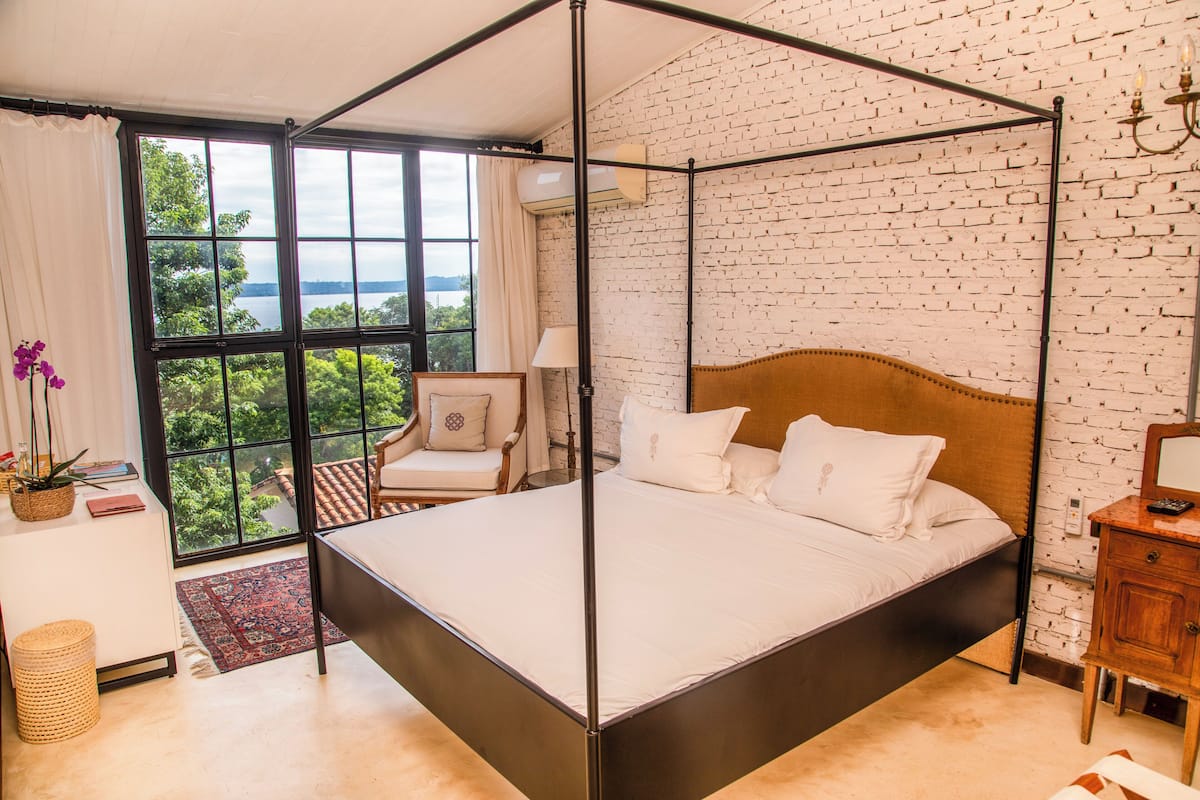 Una cama con dosel y vistas al exterior a través de amplios ventanales.