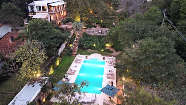 Una vista aerea di un resort con piscina, lettini e un giardino curato.