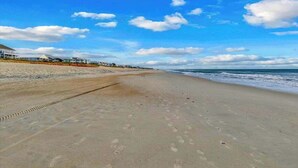 A beach with footprints, a clear sky, and buildings in the background. - Oceanfront 2BR Suite | Boardwalk-Parking-Sleeps 5 (Carolina Beach)