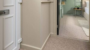 A hallway with a white door, beige walls, and a carpeted floor leading to a room with a bed, a small table, and a plant. - The Bruce's Quarter by The Wallace Monument (Stirling)