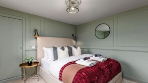 A neatly made bed with pillows, a bedside table with a plant, and a round mirror on the wall. - The Bruce's Quarter by The Wallace Monument (Stirling)