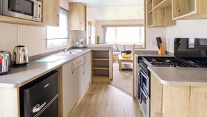 A compact kitchen with wooden cabinets, a microwave, a stove, and a sink. - Beachcombers Barmouth Bay Holiday Park (Talybont)