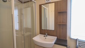 A bathroom with a glass shower enclosure, a white sink with a mirror above it, and a towel rack with a towel.