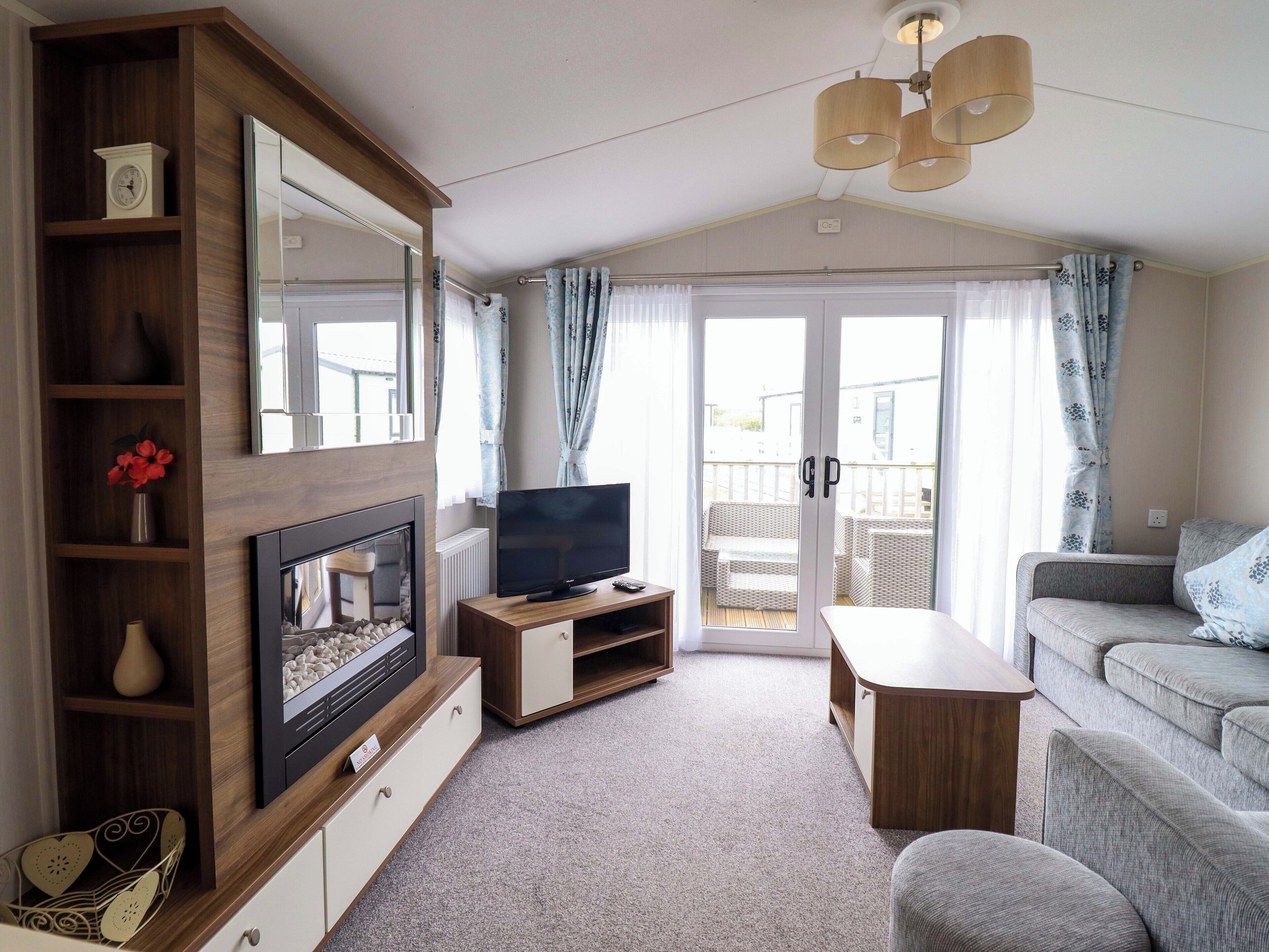 Ein Wohnzimmer mit Fernseher, Holzregalen, Kamin, Sofa und einem Balkon mit Vorhängen.
