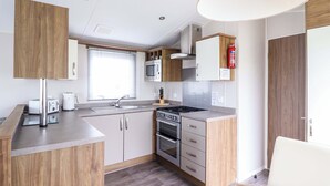 A compact kitchen with a sink, stove, microwave, and cabinets. - Sea Breeze C38 Dyffryn Seaside Estate (Dyffryn Ardudwy)