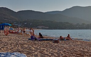 Una playa con gente relajándose, sombrillas y un flotador.