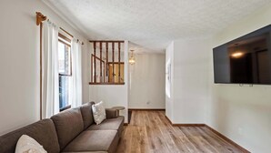 Un salon doté d’un plancher en bois, d’un canapé, d’un téléviseur fixé au mur et d’un escalier menant à un autre niveau.