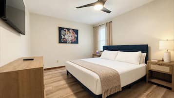 Relax in this spacious primary bedroom featuring a comfortable bed, smart TV, ceiling fan, and stylish furnishings. A peaceful retreat for a restful night's sleep after exploring Downtown Hamilton, Ohio.
