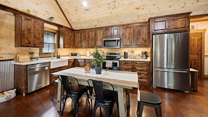 A kitchen with wooden cabinets, a stainless steel refrigerator, a microwave, and a dining table with chairs. - Little Heaven at Cloudland! (Rising Fawn)