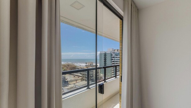 A balcony with a view of the beach and buildings. - Aptos completos em em prédio a 400m da praia \- PZO (Ilhéus)