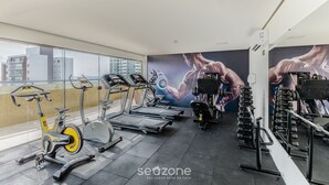 A gym with treadmills, stationary bikes, and weight machines. - Aptos completos em em prédio a 400m da praia \- PZO (Ilhéus)