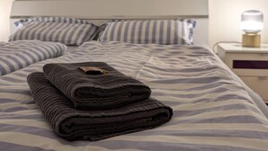 Una cama bien hecha con ropa de cama a rayas, una lámpara de noche y una ventana con una planta.