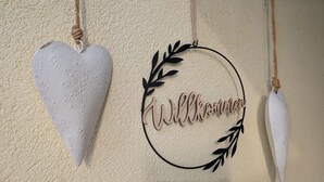 Una pared con tres adornos: un adorno con forma de corazón, un cartel que dice 'Welcome' y una pluma.