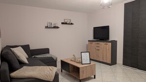 Una sala de estar moderna con un sofá gris oscuro, una mesa de centro de madera, un televisor sobre un mueble de madera y una lámpara colgante.