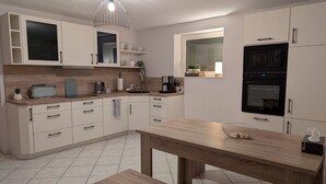 Una cocina moderna con armarios blancos, encimera de madera, horno integrado y una lámpara colgante.