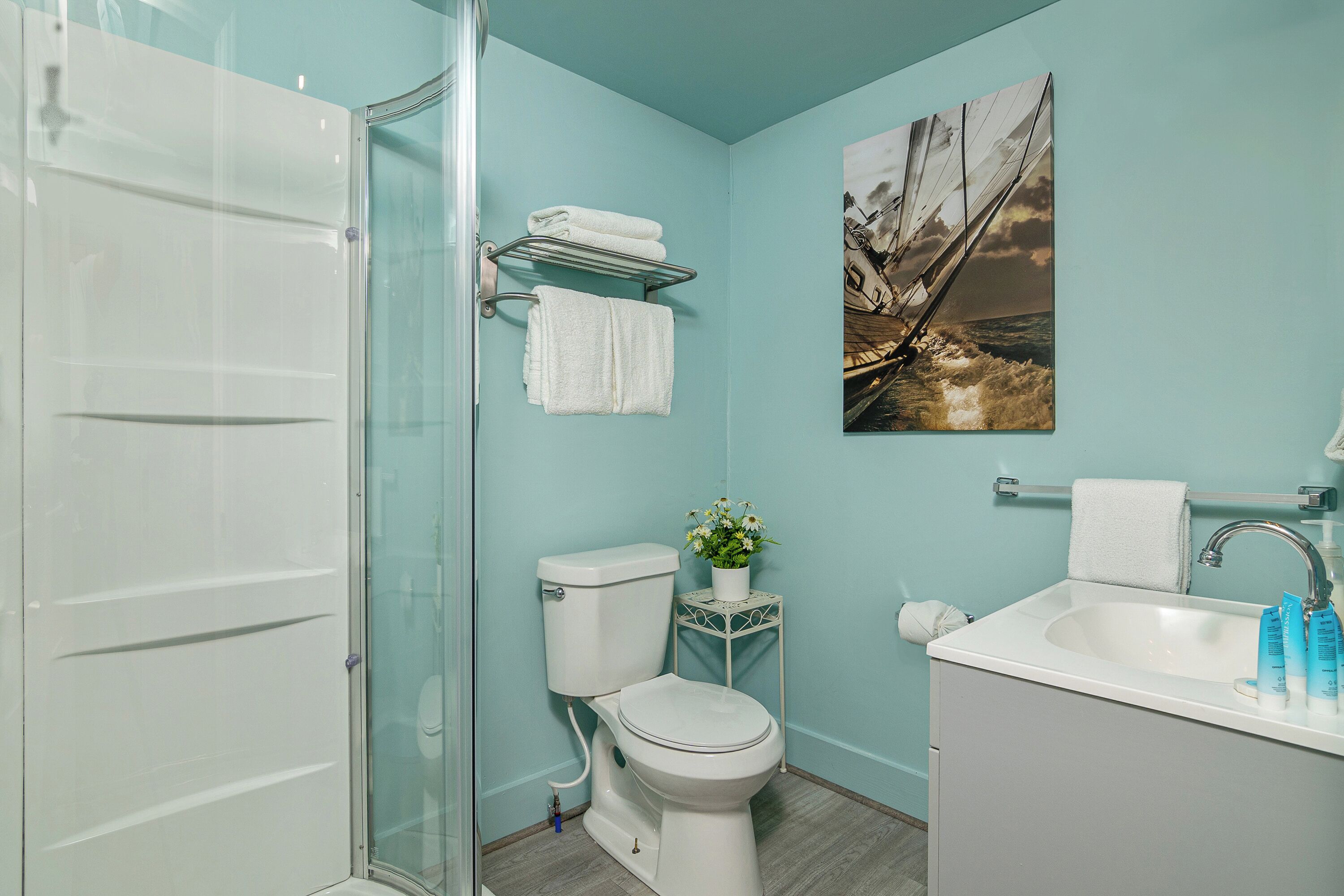 Une salle de bain avec une douche à parois de verre, des toilettes, un lavabo avec des articles de toilette et une étagère murale où sont rangées les serviettes.