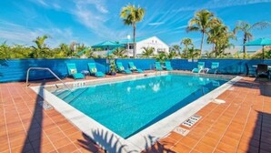A swimming pool with blue water, surrounded by a tiled deck and palm trees. - Waterfront Coconut Cottage in Fort Myers Beach (Fort Myers Beach)