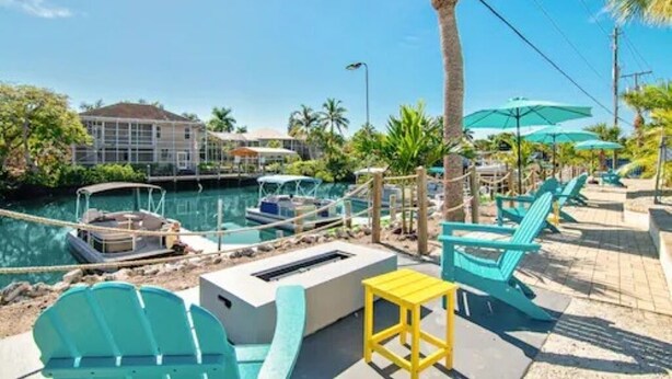 A poolside area with lounge chairs, a small table, and a boat docked by the water. - Waterfront Coconut Cottage in Fort Myers Beach (Fort Myers Beach)