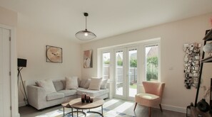A modern living room with a sectional sofa, a round coffee table, and a pink armchair. There is a large window with a view of the outdoors.