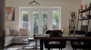 Un salon moderne avec un canapé, une table à manger et des chaises. Une grande fenêtre offre une vue sur la verdure à l’extérieur.