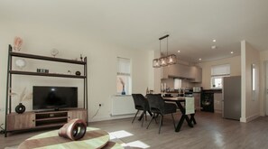 Un appartement moderne doté d’un espace de vie comprenant un téléviseur, une table à manger avec des chaises, une cuisine équipée et une grande fenêtre.