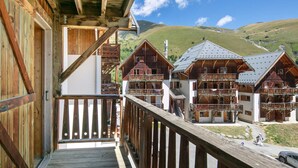 En træchalet med balkon, flere balkoner og et bjerglandskab i baggrunden.