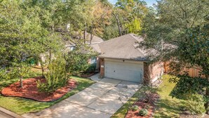 A residential house with a garage, surrounded by a well-maintained lawn and trees. - The DOVI Collection | Cozy Forest Hideaway (The Woodlands)