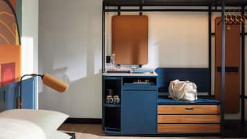 Une pièce de taille modeste comprenant un lit, un bureau avec un ordinateur, une chaise, un porte-manteau mural et un petit meuble de rangement.