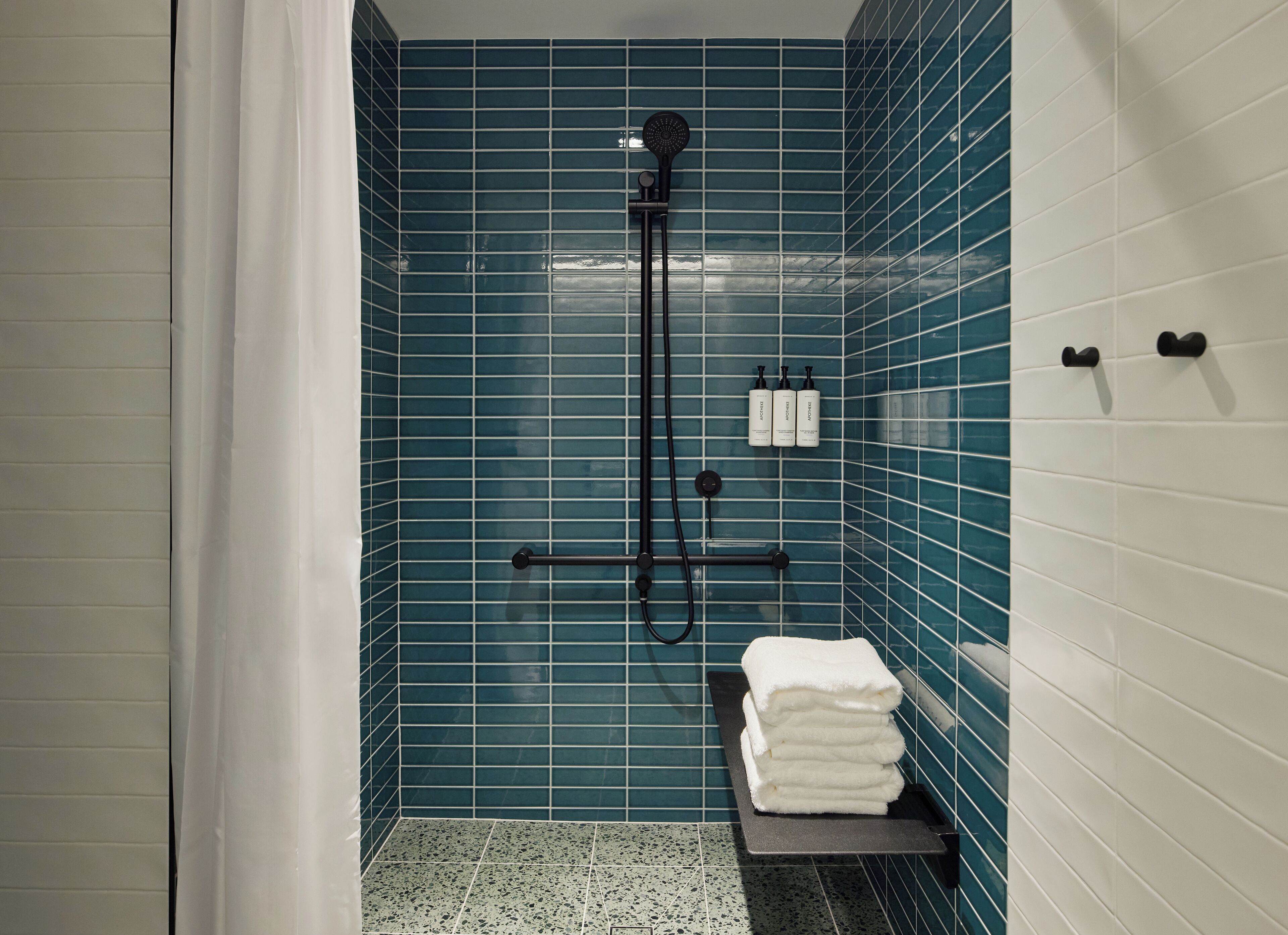 Un bagno con pareti rivestite di piastrelle blu, una doccia con un tubo nero e una pila di asciugamani bianchi su uno scaffale.