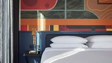 A modern hotel room with a large bed, a nightstand with a lamp, and a wall with abstract art.