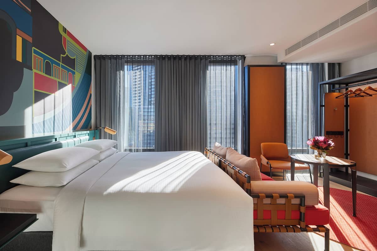 A hotel room with a large bed, a desk, a chair, and a view of the city.