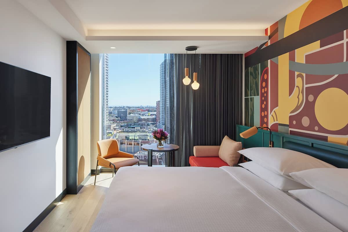A hotel room with a large bed, a seating area with a table, and a city view through the window.
