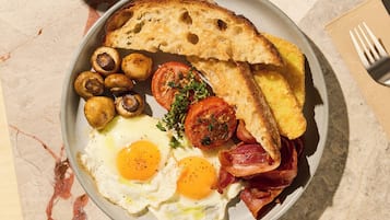 A breakfast plate with eggs, bacon, mushrooms, tomatoes, and toast on a marble table.
