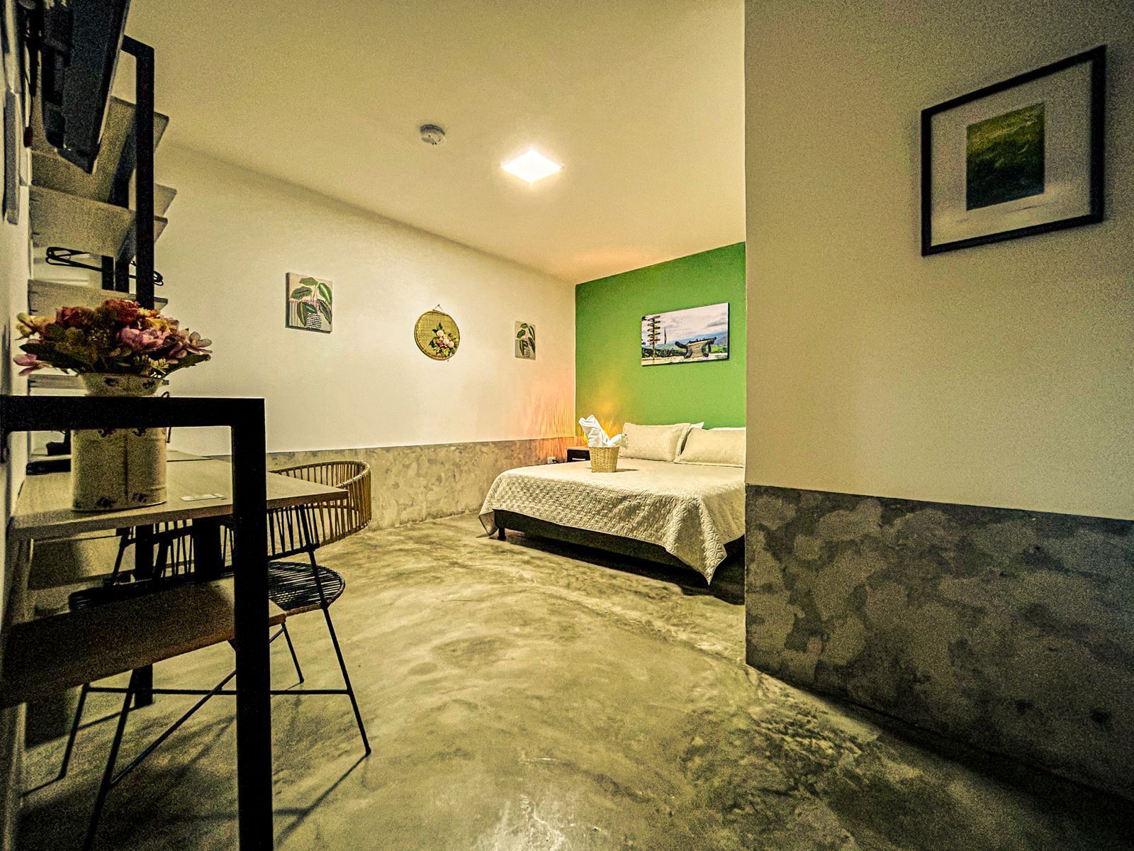 Ein Zimmer mit einem Bett, einem Esstisch mit Stühlen, einer Blumenvase und einer grünen Wand.