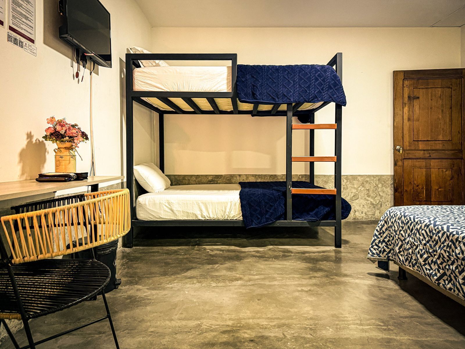 A bunk bed room with a wooden door, a small table with a vase of flowers, and a chair.