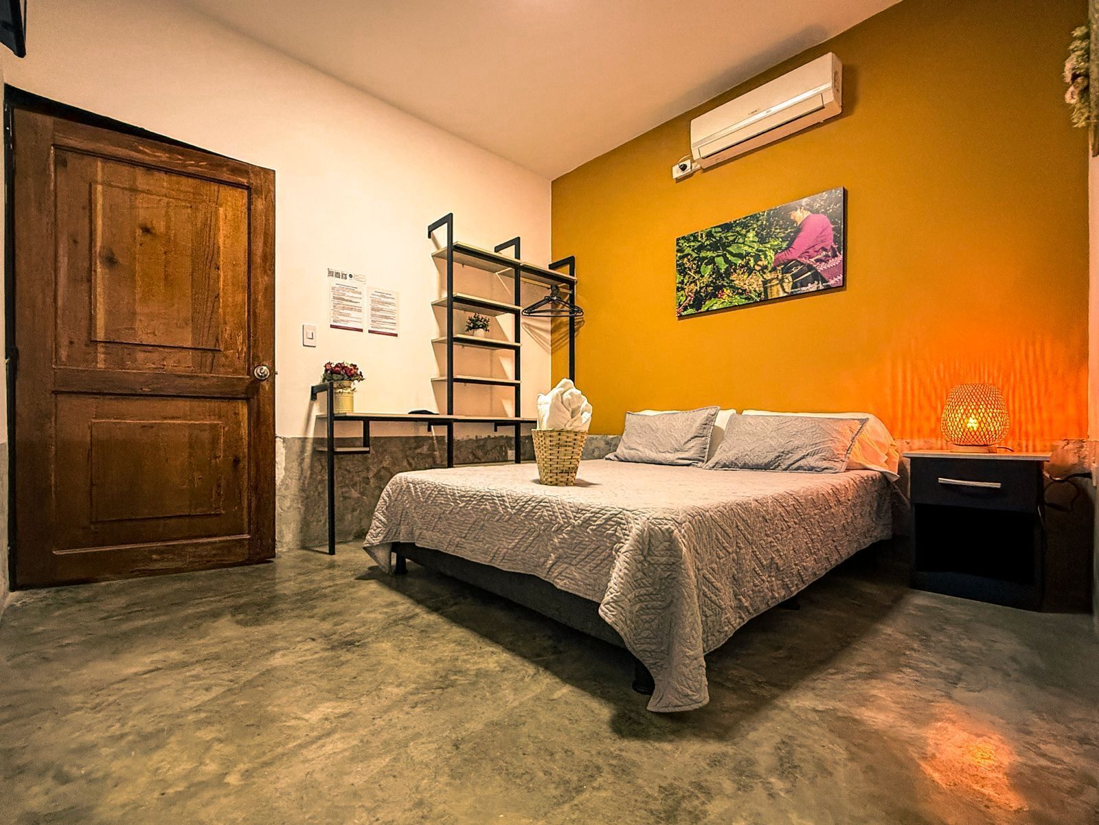 A bedroom with a bed, a wooden door, a shelf unit, an air conditioner, and a wall-mounted painting.