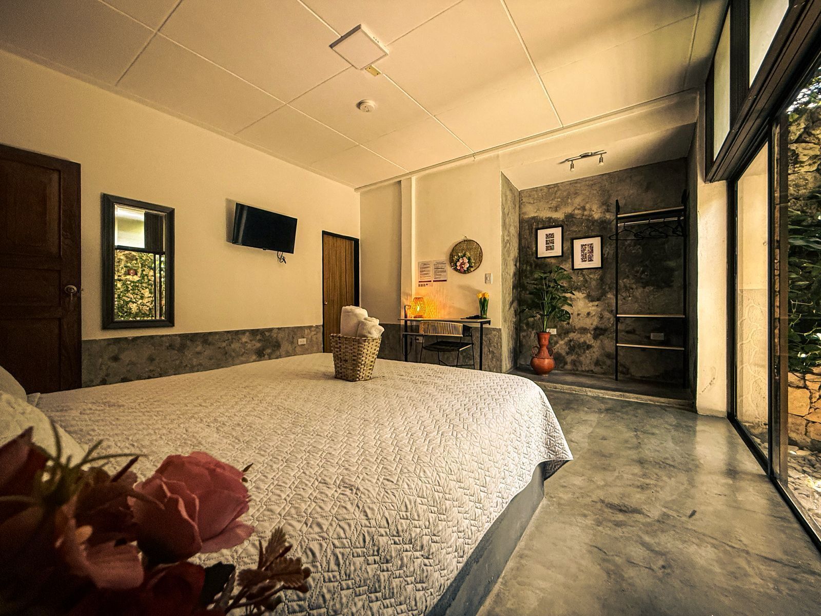 A bedroom with a large bed, a desk with a chair, a television, and a stone wall.