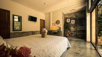 A bedroom with a large bed, a desk with a chair, a television, and a stone wall.