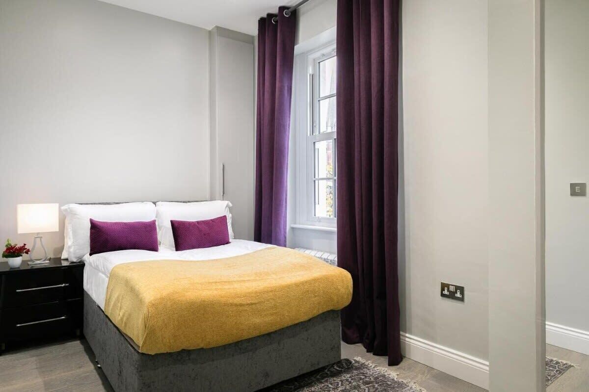 Une chambre à coucher avec un lit, une table de chevet, une lampe et des rideaux violets.