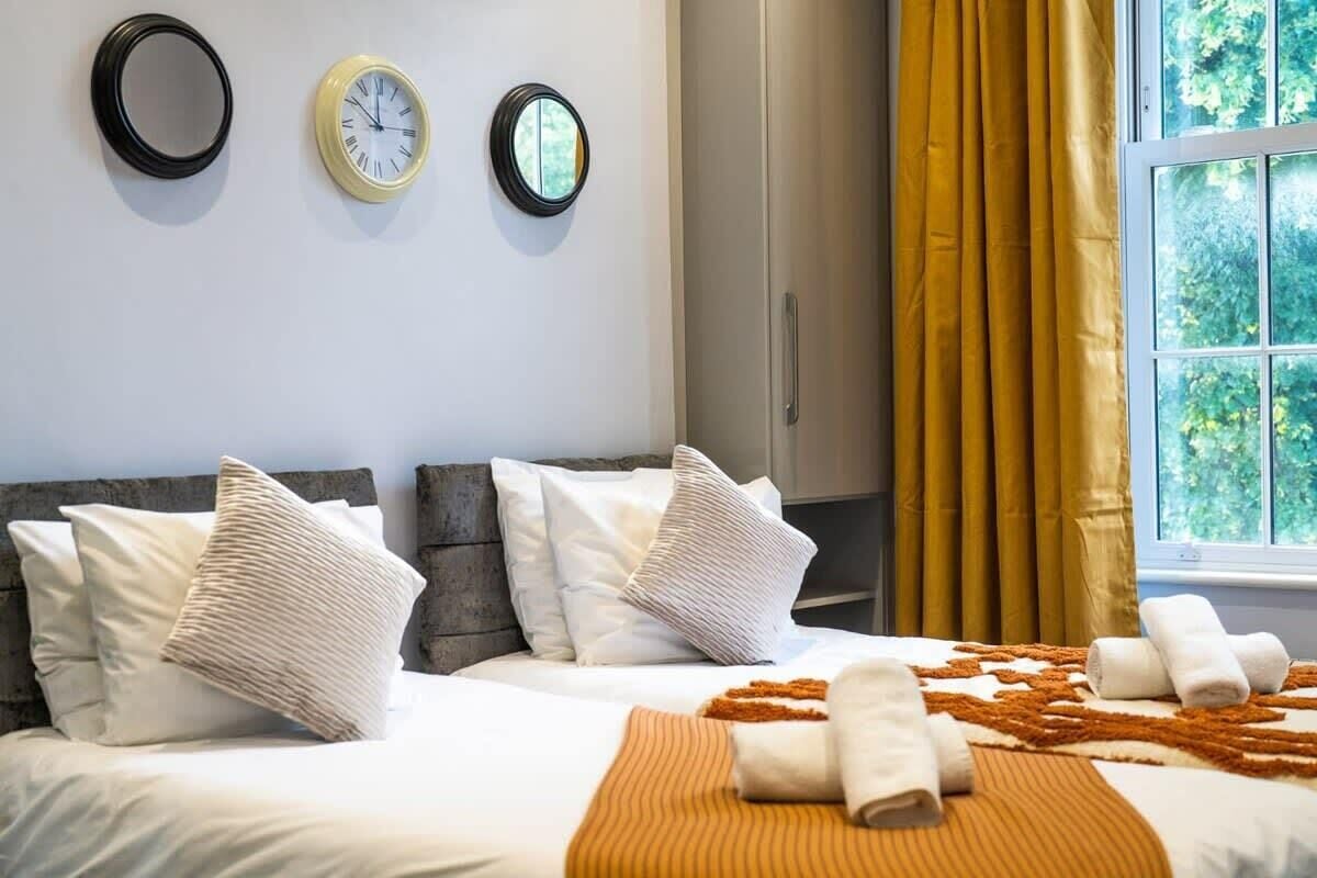 Une chambre d’hôtel avec deux lits, une fenêtre avec des rideaux jaunes et trois horloges murales.